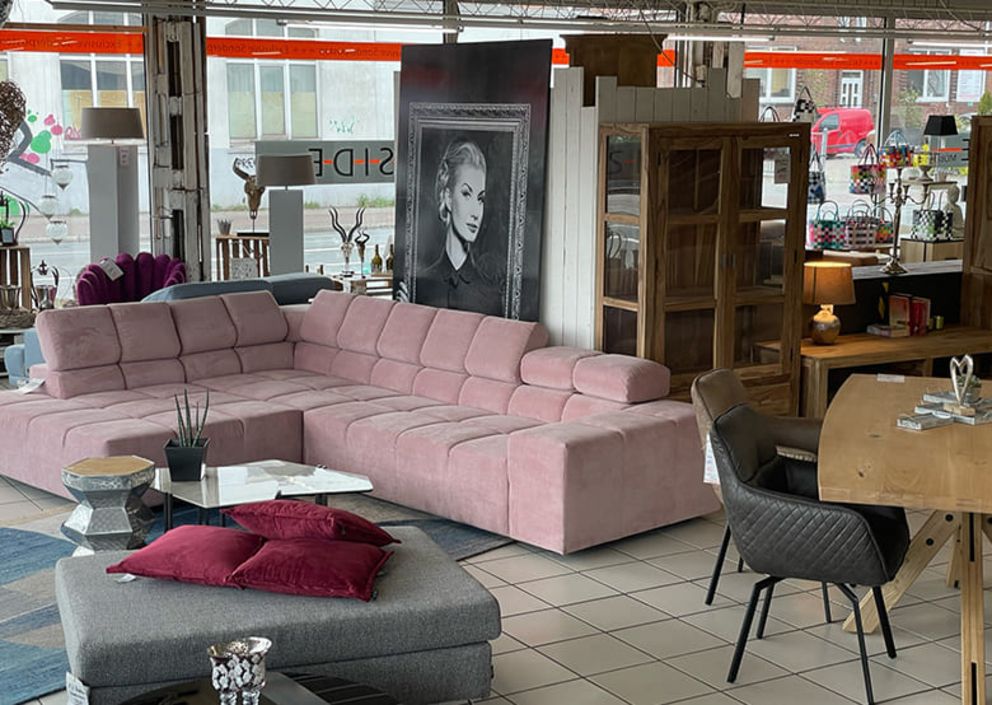 Mehrere Möbelstücke wie ein großes Bild und eine rosa Wohnlandschaft stehen in einem Ausstellungsraum